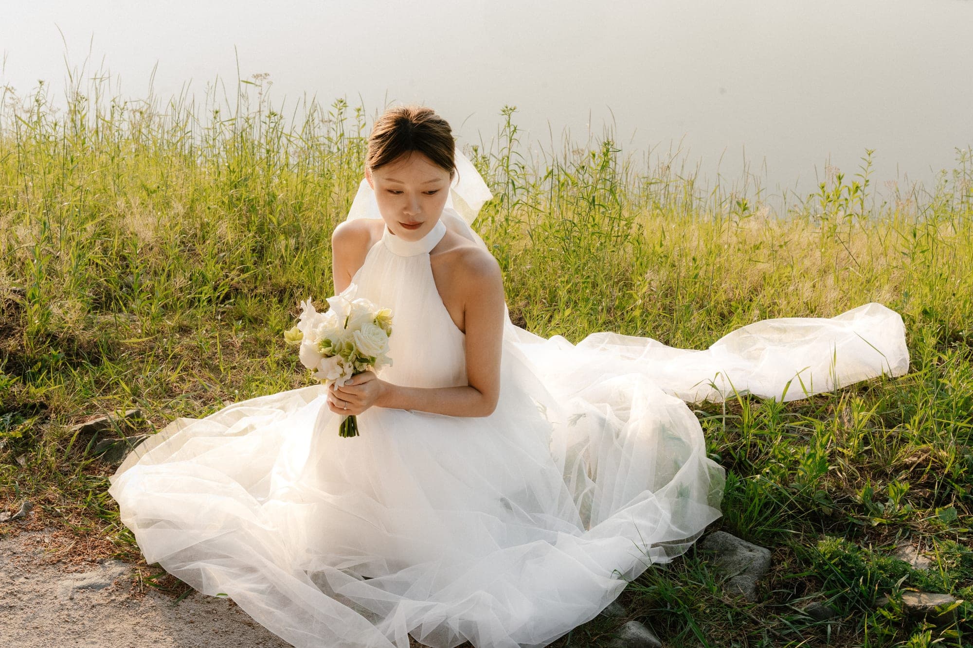 물가 수풀에 앉아 부케를 든 신부